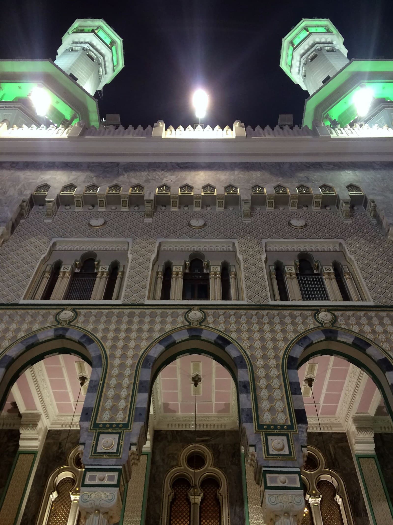 Gece Mescid-i Haram 1 No'lu kapısının geometrik desenli cephesi, kemerleri ve yeşil ışıklı minareleri, dikey kadraj
