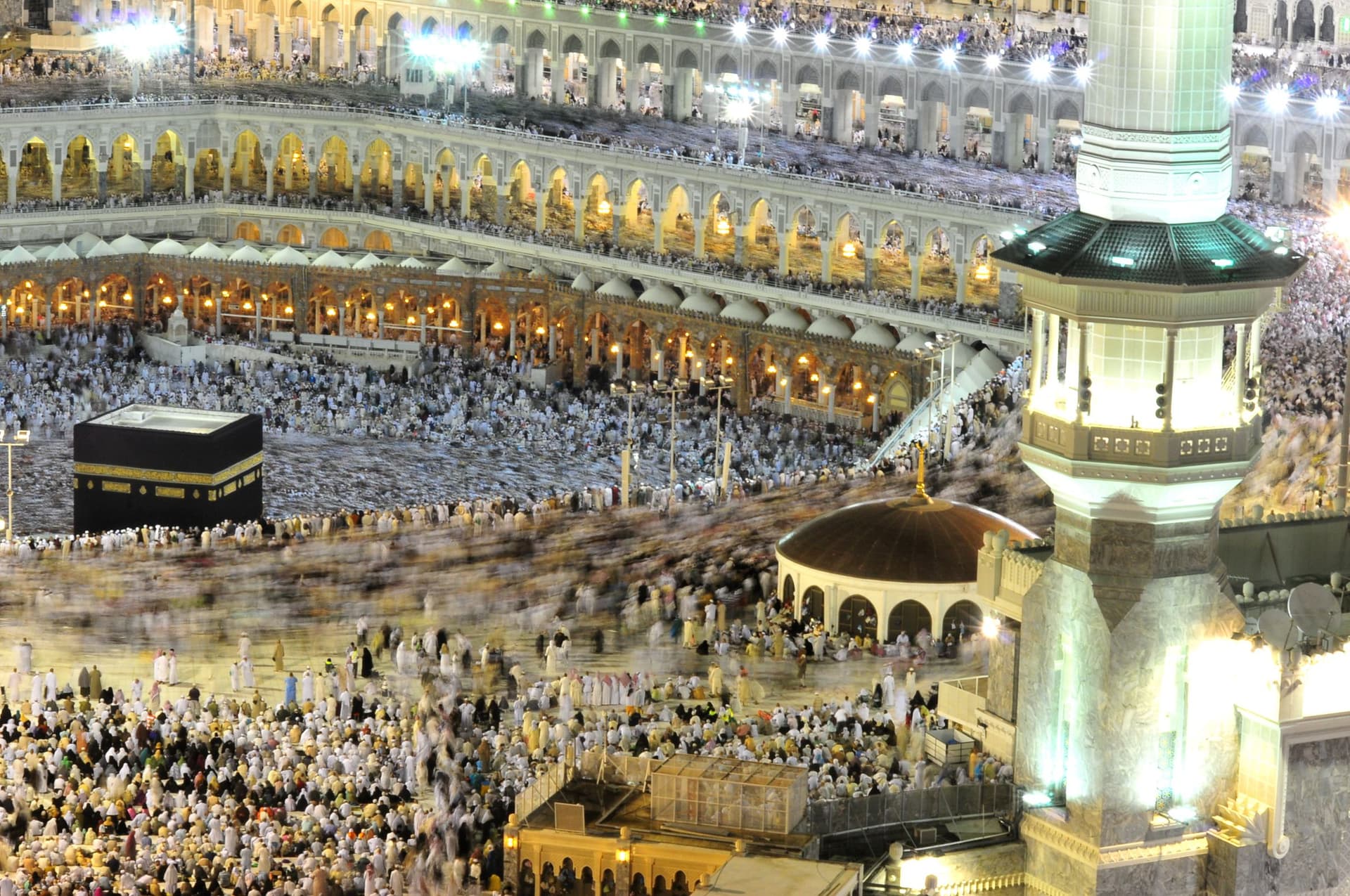 Akşam ışıklarıyla aydınlanan Mescid-i Haram'da Kâbe'nin etrafında tavaf eden hacılar ve minare